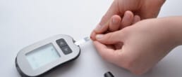 A person using a blood glucose meter to check their blood sugar level by placing a drop of blood on a test strip