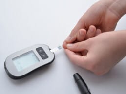 A person using a blood glucose meter to check their blood sugar level by placing a drop of blood on a test strip