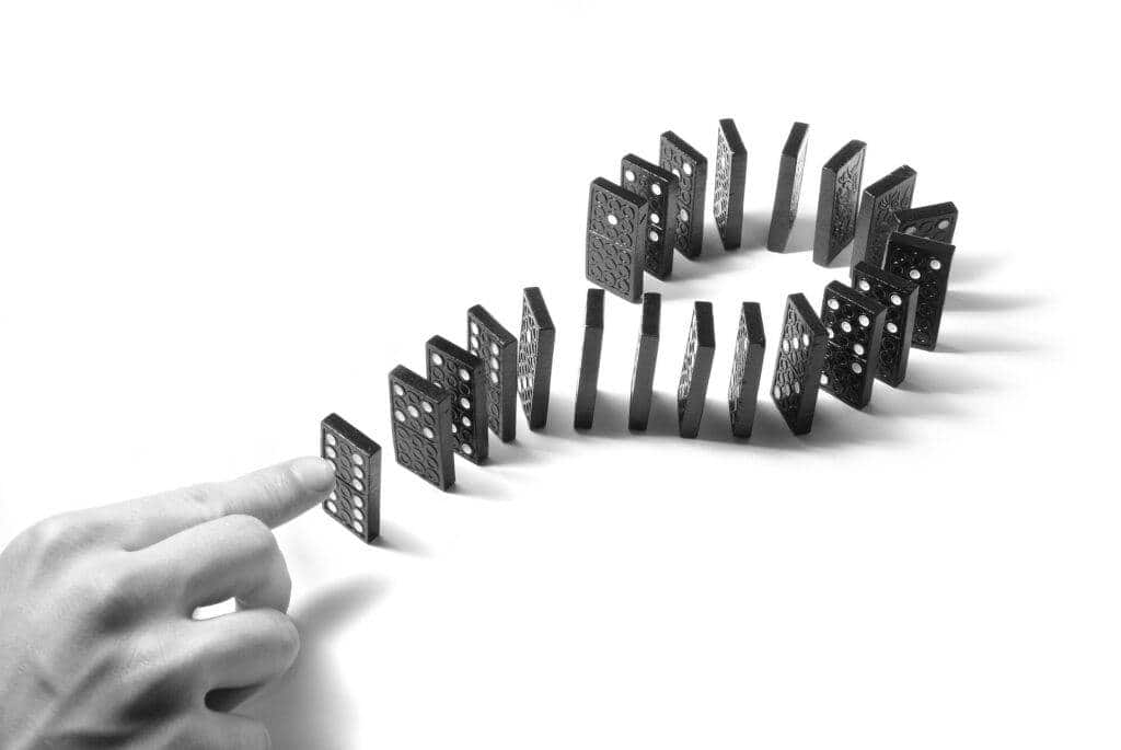 A hand about to push the first tile in a circle of standing dominoes - symbolising the domino effect and how one small action can trigger a chain reaction