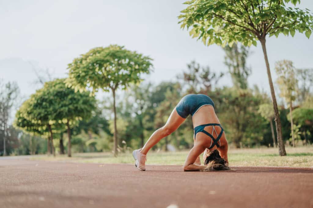 Woman in athletic wear practicing a forearm-supported yoga stretch outdoors on a park pathway, surrounded by trees.