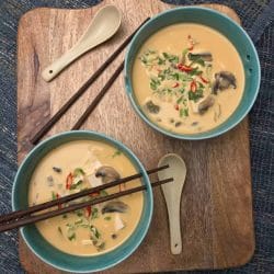 Mushroom Soup in 2 green bowls kept on a wooden board with 1 set of chopsticks over 1 bowl and 1 set of chopsticks beside the bowls kept on the board