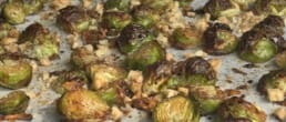 Close-up of roasted Brussels sprouts on a baking sheet, mixed with small pieces of toasted walnuts and lightly browned for a crispy texture.