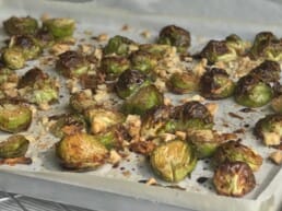 Close-up of roasted Brussels sprouts on a baking sheet, mixed with small pieces of toasted walnuts and lightly browned for a crispy texture.