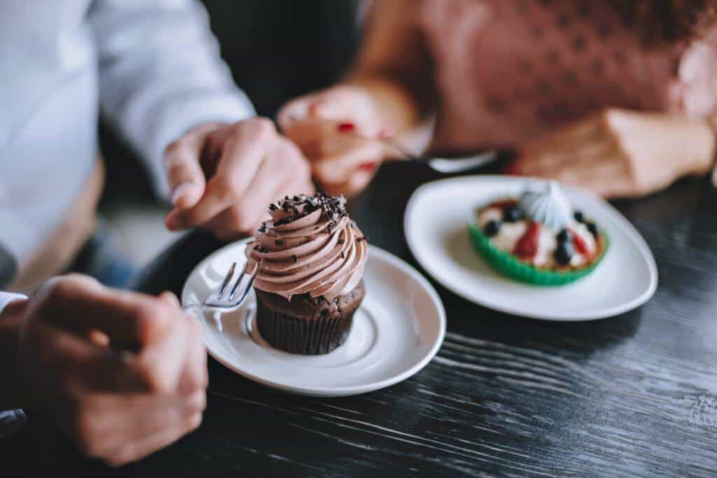 Two people about to enjoy desserts - a rich chocolate cupcake and a fruit tart - symbolising sweet cravings and indulgent eating habits